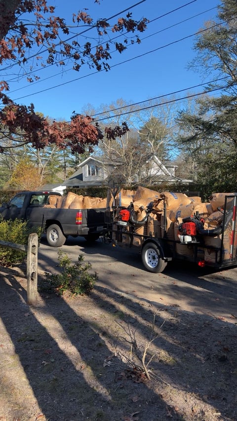 Dark SUV with wood chipper trailer parked on residential street with autumn trees and house in background