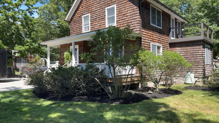 Red shingle house with white porch and columns surrounded by manicured shrubs and green lawn
