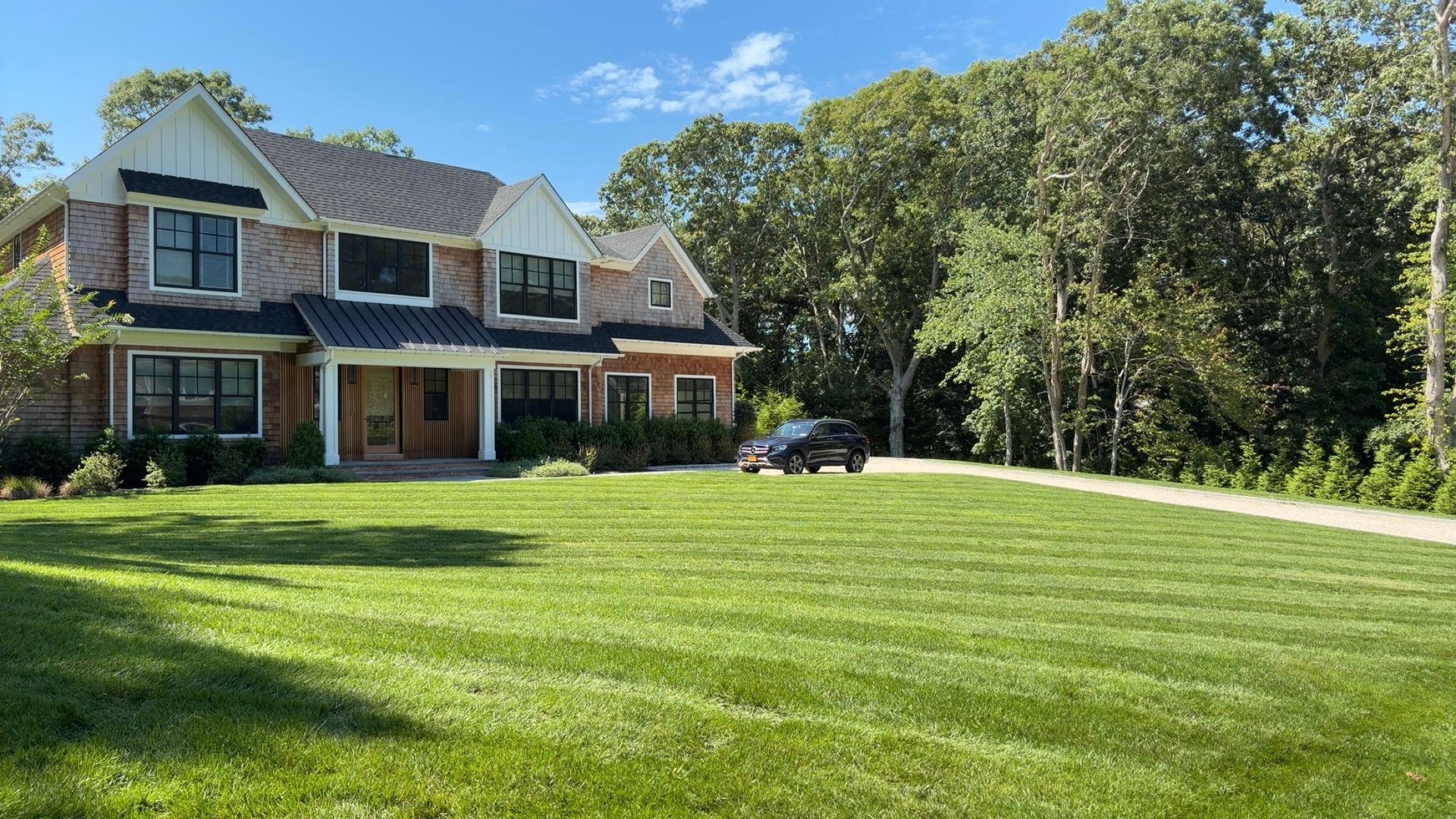 Large two-story brick and siding home with driveway, set on manicured lawn surrounded by mature trees